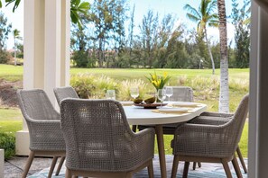 An outdoor dining area with wicker chairs and a round table, set against a backdrop of a golf course and trees. - Treasure Retreat 3 bed Villa, Kings, Stylish Remodel (Waikoloa Village)