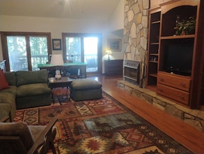 A living room with a stone fireplace, a television, and a green sofa. - 4 BR Mountain Retreat in Stunning Hardwood Forest: Big Views & Friendly Goats (Blairsville)