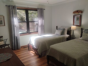 A bedroom with two beds, a window with curtains, a bedside table with a lamp, and a framed picture on the wall. - 4 BR Mountain Retreat in Stunning Hardwood Forest: Big Views & Friendly Goats (Blairsville)