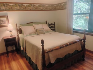 A bedroom with a wooden four-poster bed, a nightstand with a lamp, and a window with a view of trees. - 4 BR Mountain Retreat in Stunning Hardwood Forest: Big Views & Friendly Goats (Blairsville)