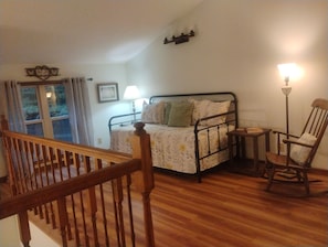 A bedroom with a wooden bed, a nightstand, a chair, a lamp, a window with curtains, and a staircase. - 4 BR Mountain Retreat in Stunning Hardwood Forest: Big Views & Friendly Goats (Blairsville)