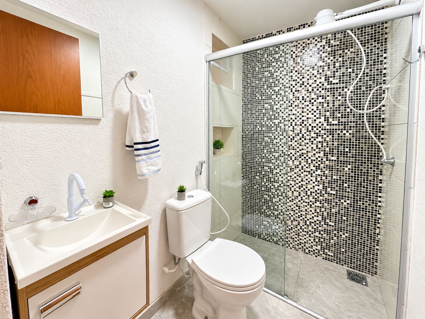 Un baño moderno con un lavamanos blanco, un inodoro y una ducha con un revestimiento de mosaicos.