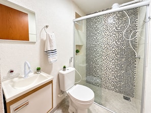 Un baño moderno con un lavamanos blanco, un inodoro y una ducha con un revestimiento de mosaicos.