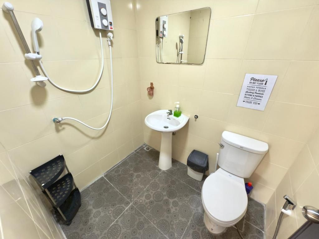 A bathroom with a toilet, sink, and shower. There is a sign on the wall and a small trash bin.