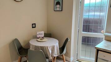 A dining area with a round table, four chairs, a clock, a framed picture, and a washing machine.