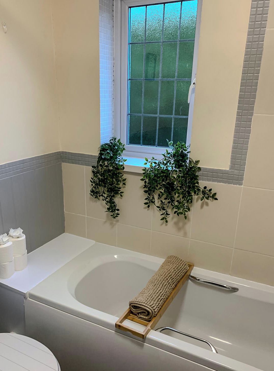 A bathroom with a bathtub, a window, and two wall-mounted plants.