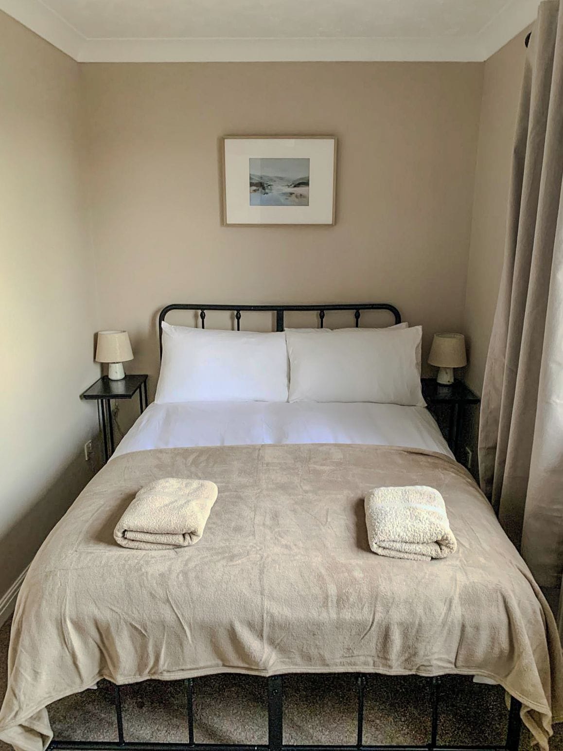A single bed with a headboard, two bedside lamps, a framed picture on the wall, and two towels on the bed.