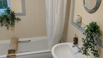 A bathroom with a bathtub, a sink, a mirror, and two potted plants.