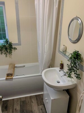 A bathroom with a bathtub, a sink, a mirror, and two potted plants. - Cosy house 5 mins walk from the sea. (Cleethorpes)