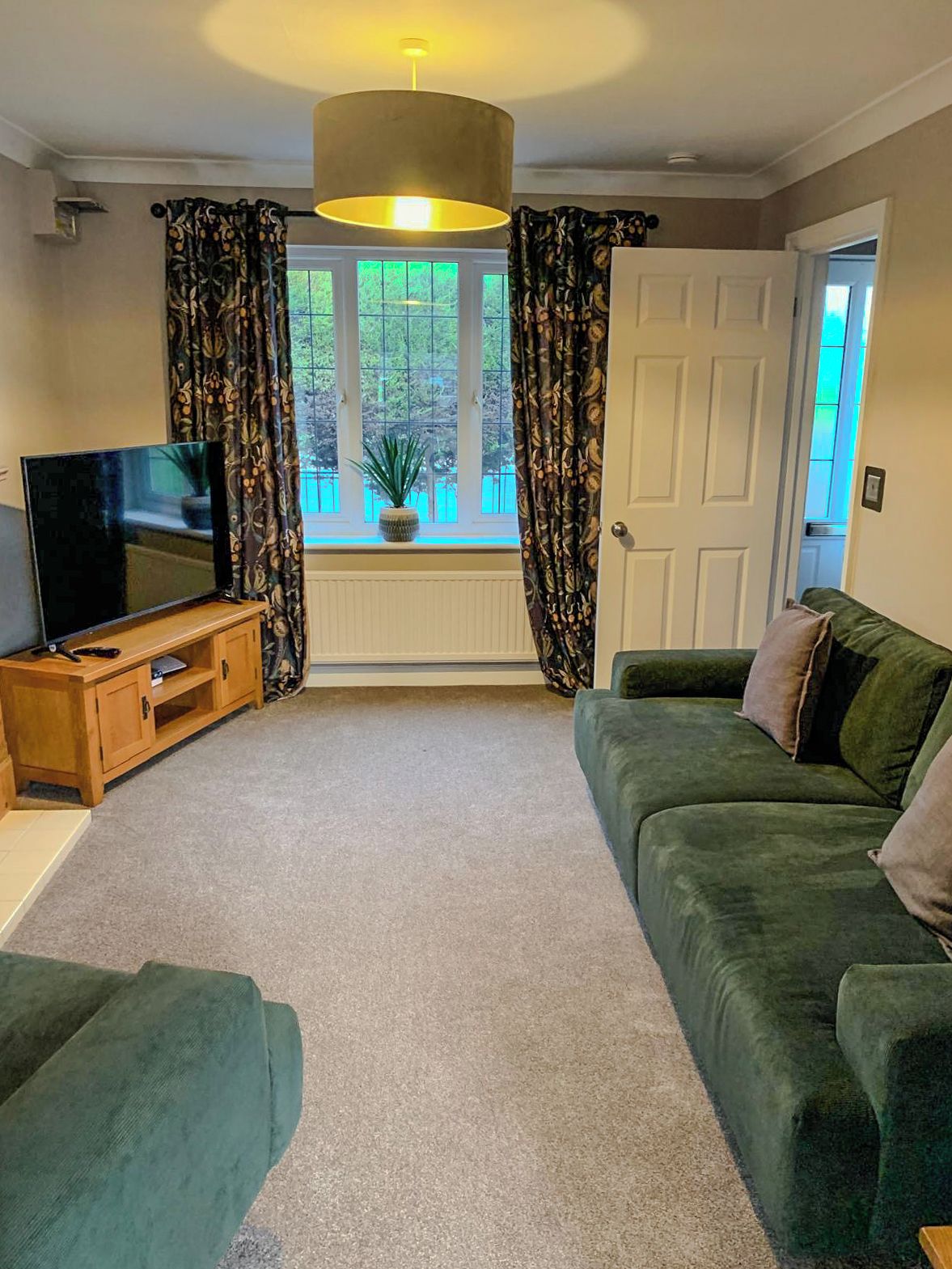 A living room with a television, a sofa, a wooden cabinet, and a window with curtains.