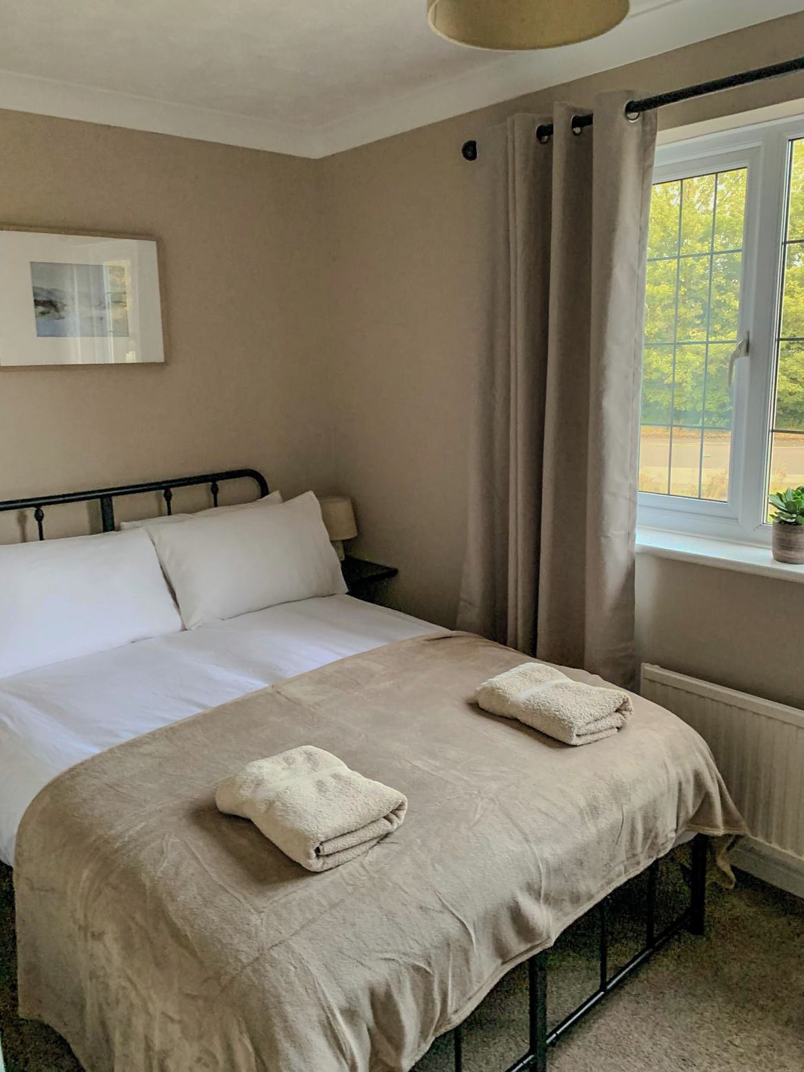 Una cama individual con cabecera, una mesita de noche y una ventana con cortinas.