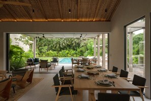 Espaço de refeições com vista para uma piscina e vegetação exuberante.