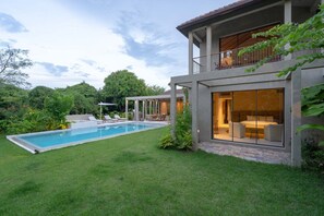 Ein modernes Haus mit Swimmingpool, Sitzgelegenheiten im Freien und einer großen Glasdoor, die zu einem Schlafzimmer führt.
