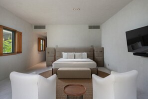 Ein modernes Schlafzimmer mit einem großen Bett, zwei weißen Sessel, einem kleinen runden Tisch und einem an der Wand befestigten Fernseher.