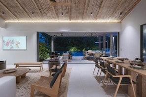 A modern dining area with a large table and chairs, a ceiling with a woven pattern, and a view of greenery outside. - Villa Armonía - Selva, Las Palmas - Punta Mita (Punta Mita)