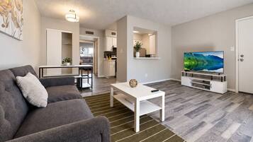 A modern living room with a grey sofa, a white coffee table, and a flat-screen TV on a stand.