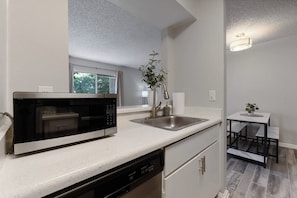 A compact kitchen with a built-in microwave, a sink, and a small table with chairs. - Pool | Gym | Great For Mid/Long Stays (Mesa)