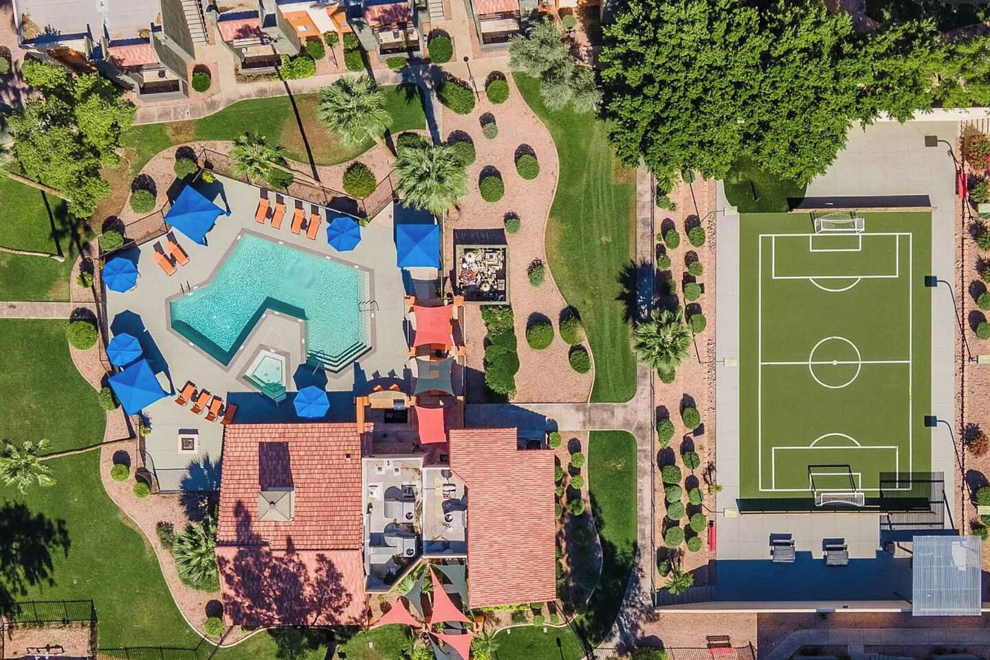An aerial view of a resort with a swimming pool, lounge areas, and a soccer field.