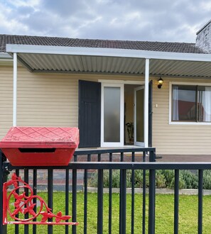 A residential building with a covered porch, a sliding glass door, and a small garden area. - Ferguson House – Cosy Hunter Valley Escape (Cessnock)