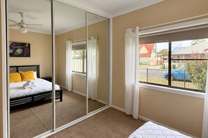 Quarto com cama, ventilador de teto, janela com cortinas e vista para o exterior.