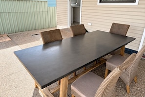 A rectangular outdoor table with four chairs, set against a house with siding and a window above. - Ferguson House – Cosy Hunter Valley Escape (Cessnock)
