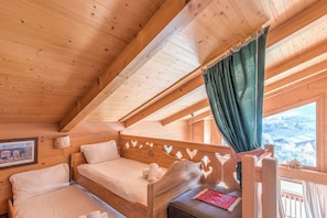A wooden cabin bedroom with a bed, a small table, and a window with curtains. - Le Panorama Montagnard - Welkeys (Combloux)