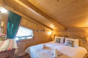 A wooden cabin room with a bed, a window with curtains, a wall-mounted lamp, and a small table with a plant. - Le Panorama Montagnard - Welkeys (Combloux)