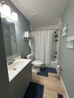 A bathroom with a sink, toilet, and shower area. There are towels on a rack and a shower curtain. - Cozy 2-bedroom house in peaceful Speedway close to the track! (Speedway)