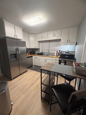 A modern kitchen with white cabinets, stainless steel appliances, and a wooden dining table. - Cozy 2-bedroom house in peaceful Speedway close to the track! (Speedway)