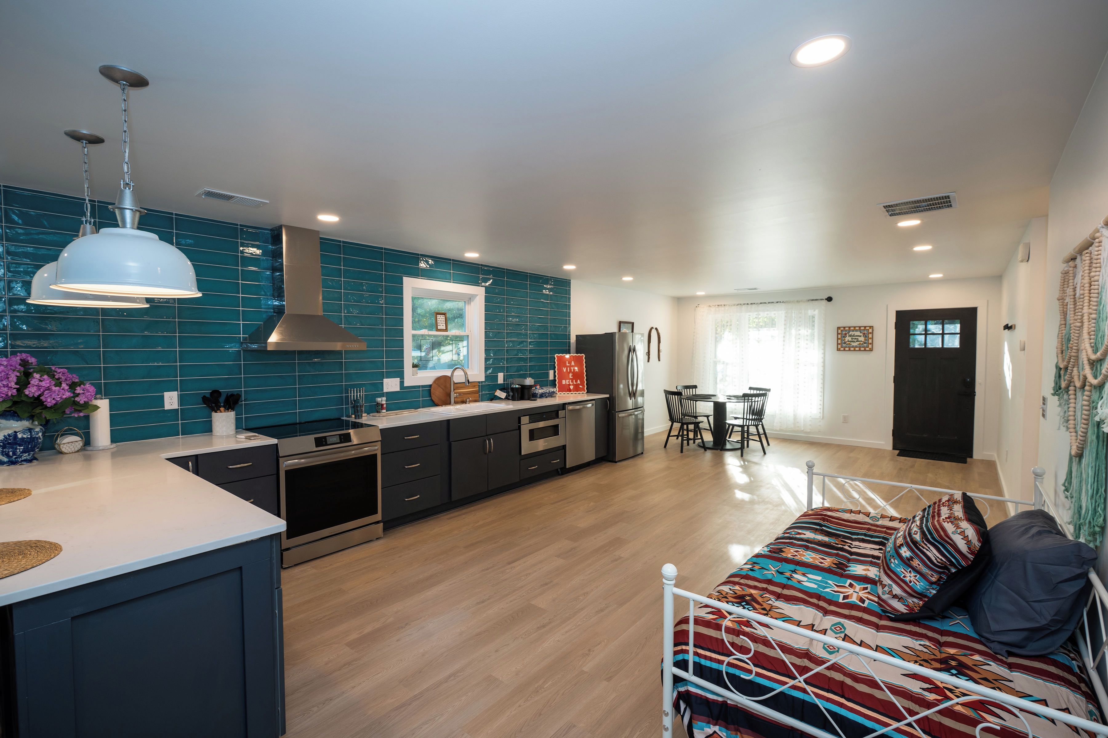 A modern kitchen with a central island, stainless steel appliances, and teal backsplash.