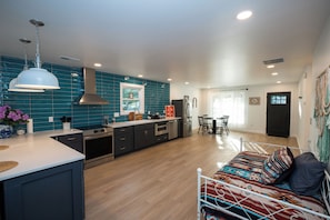 Une cuisine moderne dotée d’un îlot central, d’appareils électroménagers en acier inoxydable et d’un pare-feu turquoise.