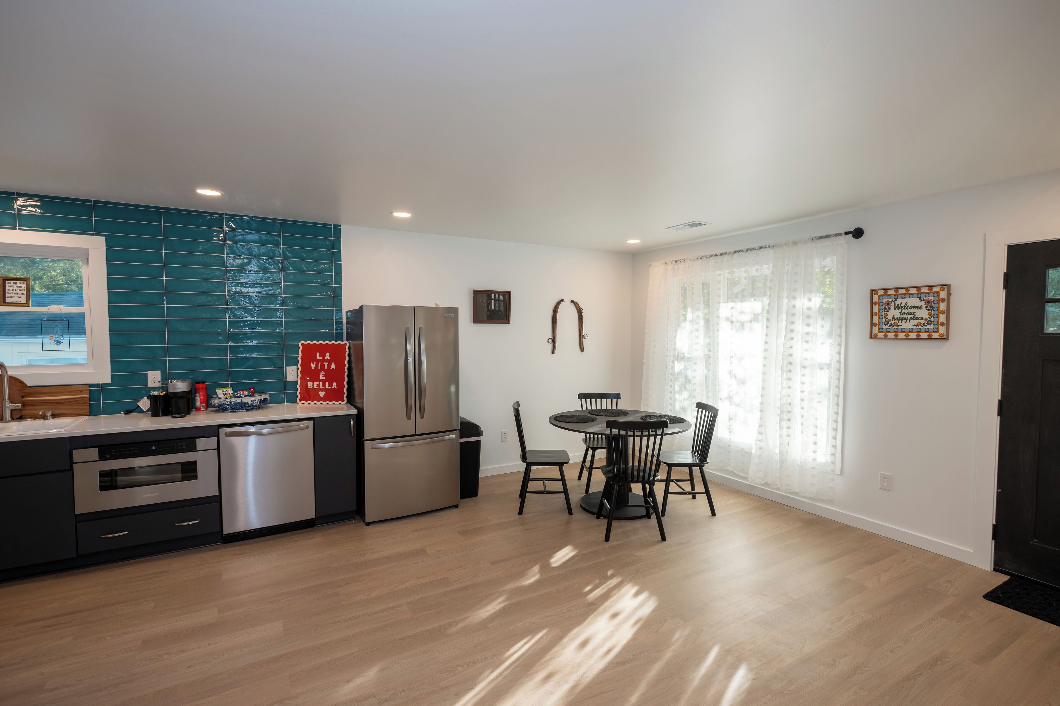 Una cocina moderna con refrigerador de acero inoxidable, lavavajillas y pileta. Hay una zona de comedor con mesa redonda y sillas.