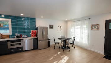 Una cocina moderna con refrigerador de acero inoxidable, lavavajillas y pileta. Hay una zona de comedor con mesa redonda y sillas.