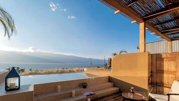 A pool area with steps leading to a lounge, overlooking a body of water and mountains.