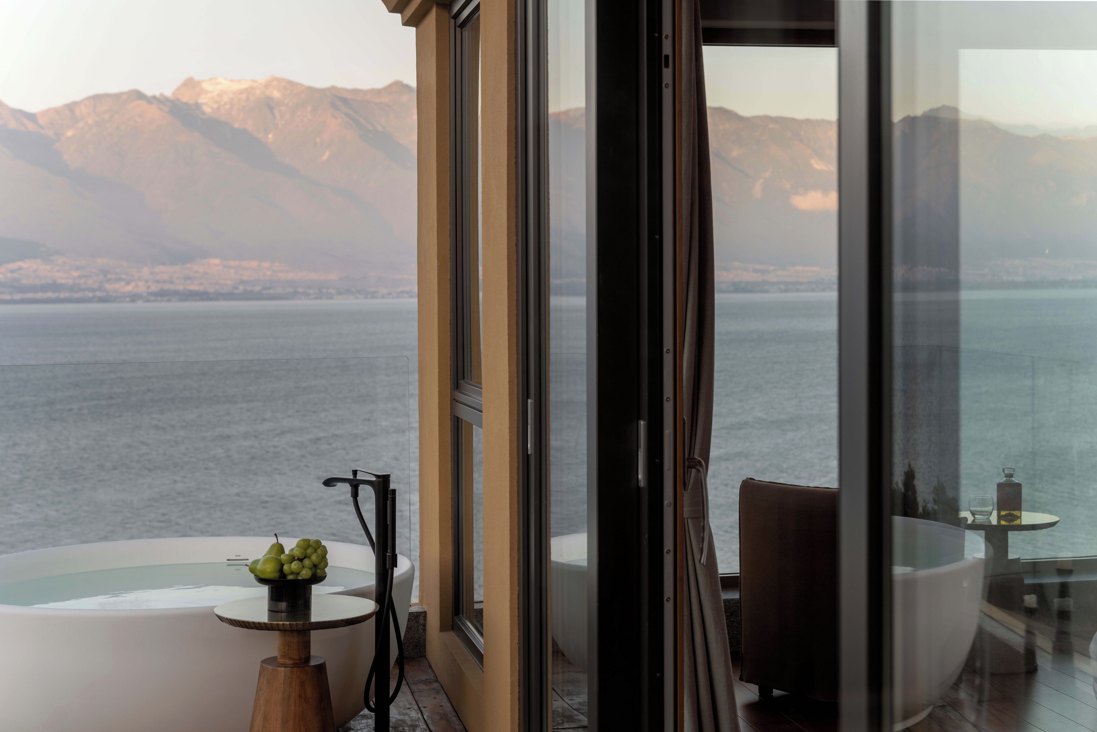 A modern interior with a glass balustrade overlooking a body of water and mountains.