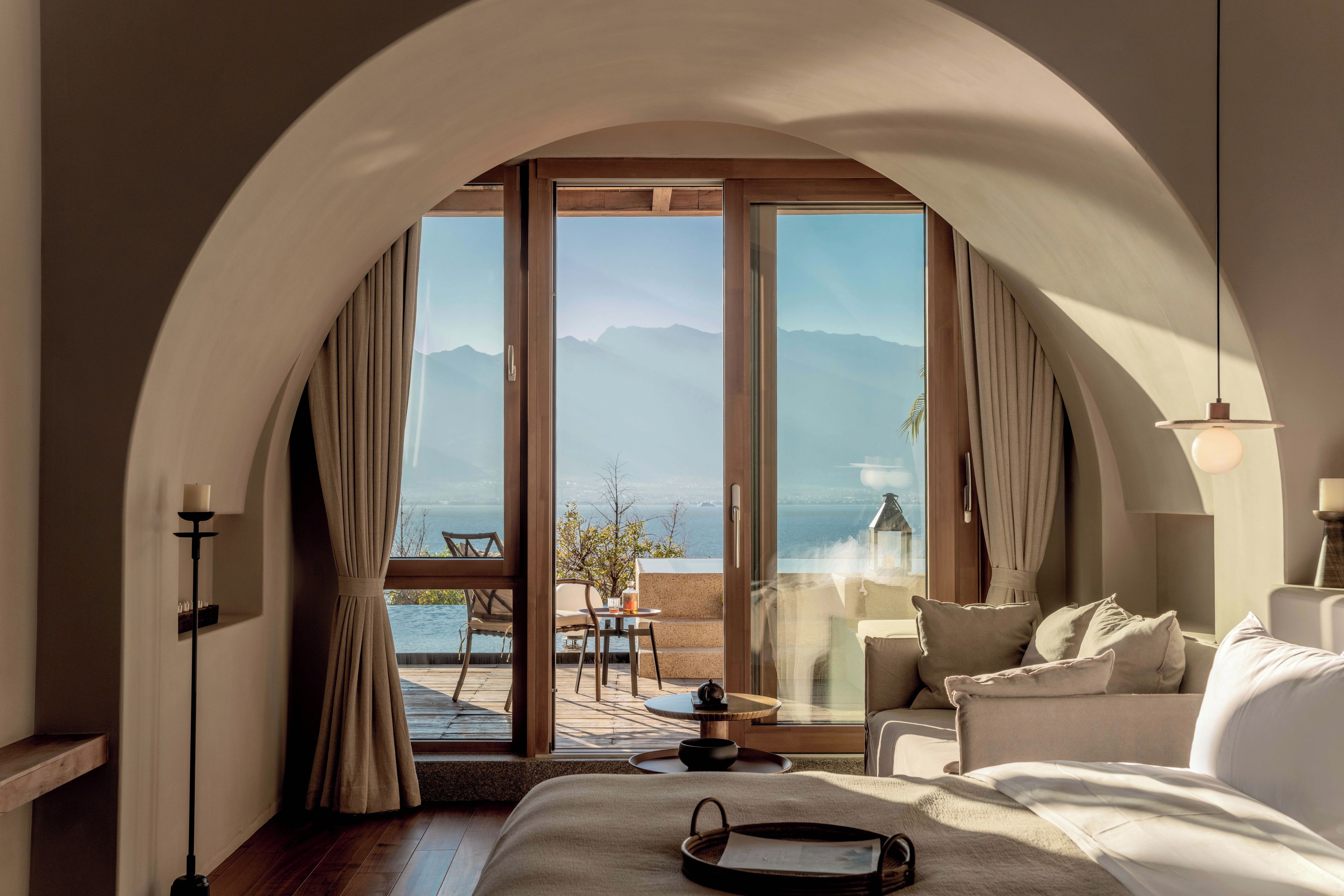 A hotel room with a large arched doorway leading to a balcony with a view of the sea and mountains.