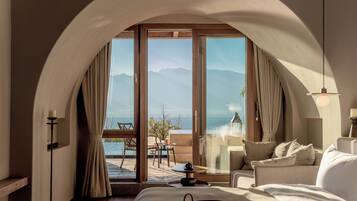 A hotel room with a large arched doorway leading to a balcony with a view of the sea and mountains.