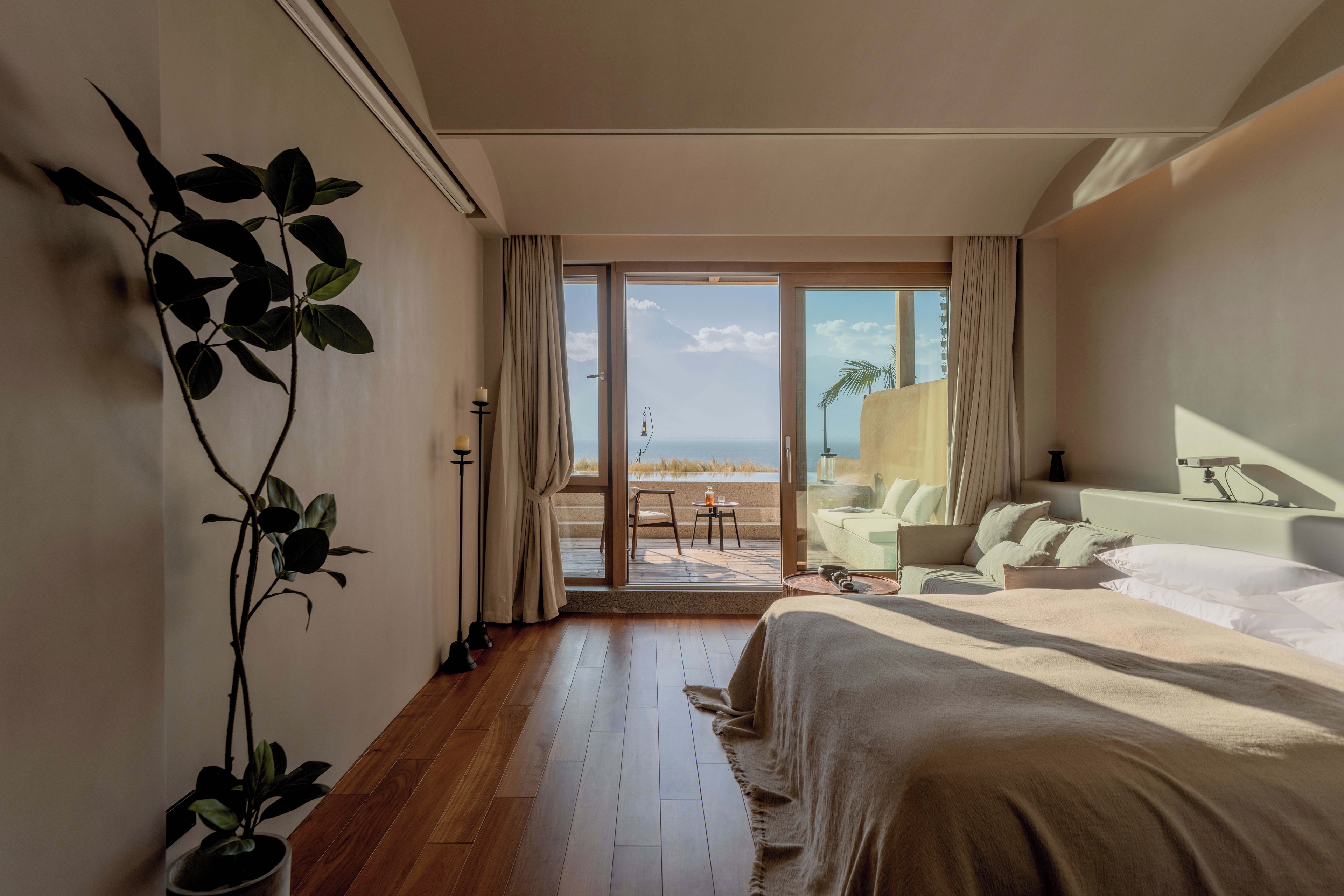 Habitación de hotel con una cama grande, zona de estar y vistas a la playa, además de una planta en maceta.