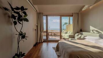 Habitación de hotel con una cama grande, zona de estar y vistas a la playa, además de una planta en maceta.