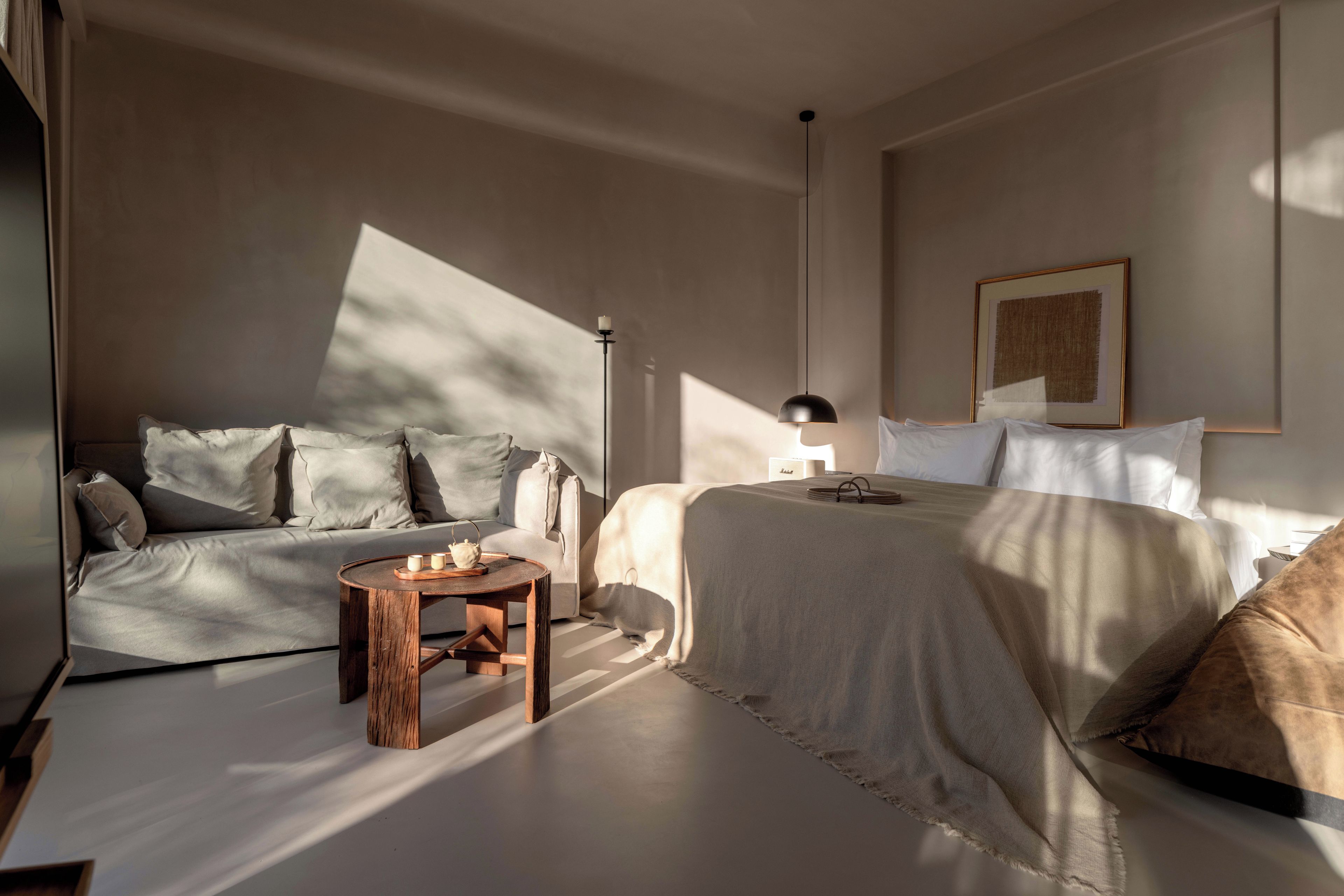 A bedroom with a bed, a sofa, a small wooden table, and a floor lamp.