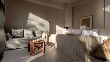 A bedroom with a bed, a sofa, a small wooden table, and a floor lamp.