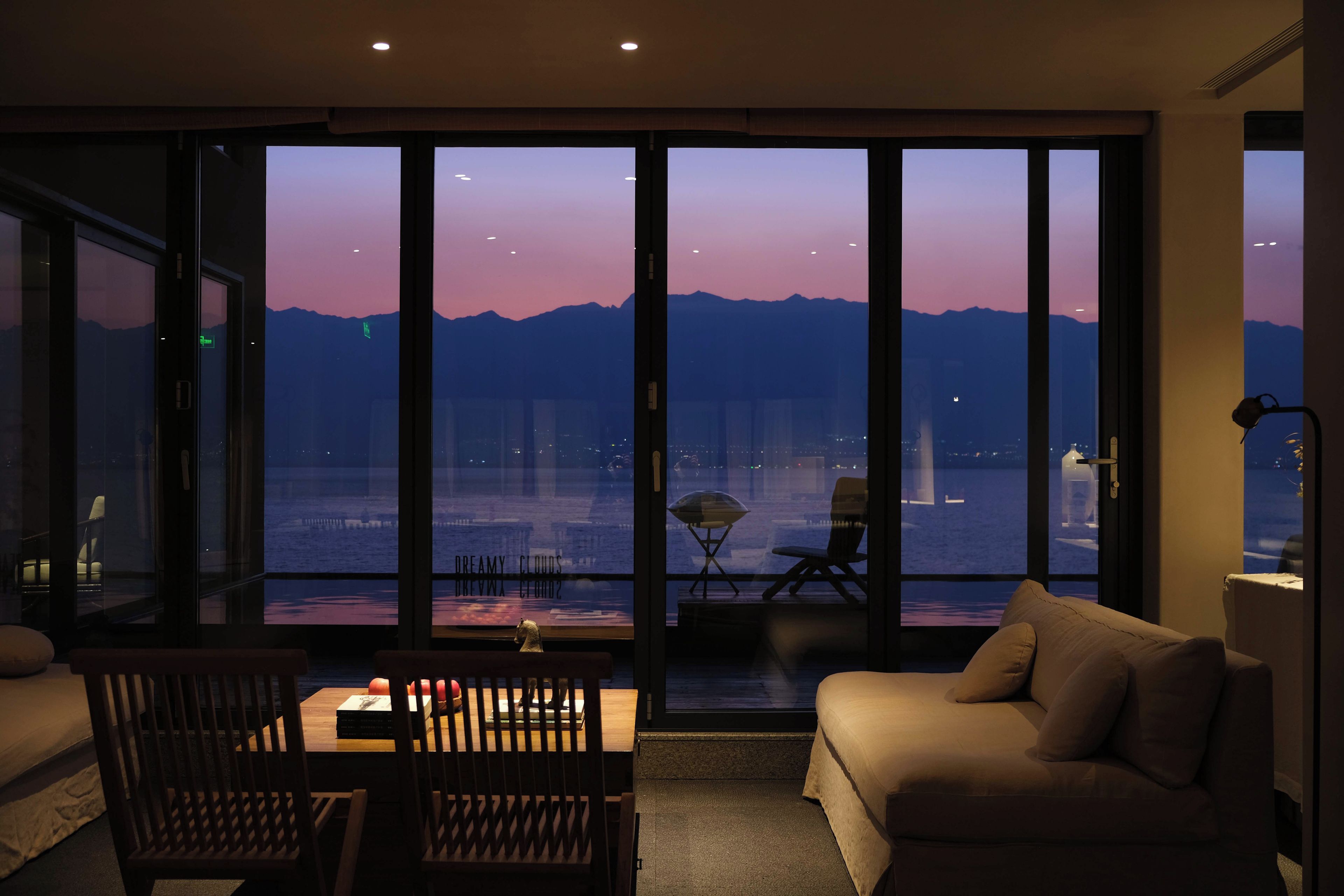 Una habitación con un gran ventanal corredero que da a un balcón con vistas a un cuerpo de agua y montañas.