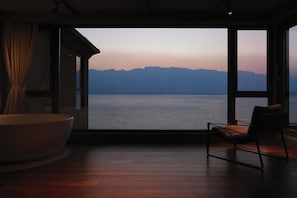 A room with a large window offering a view of a body of water and distant mountains. - Liuzhao Mountain View Holiday Hotel (Dali)