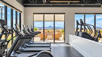 Un gimnasio con múltiples cintas de correr, una zona de estar con vistas a las montañas y grandes ventanales.