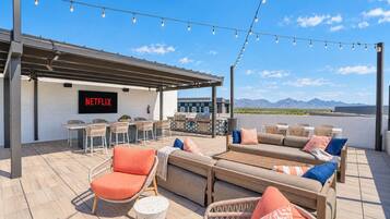 A rooftop patio with outdoor seating, a bar area, and a TV screen displaying 'NETFLIX'.