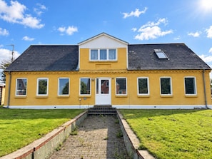 A two-story yellow building with a central entrance, multiple windows, and a paved pathway leading to the door. - 4 Person Holiday Home in Struer (Struer)