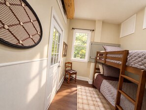 Une chambre avec un lit superposé, une chaise, une fenêtre donnant sur des arbres et un objet décoratif fixé au mur.