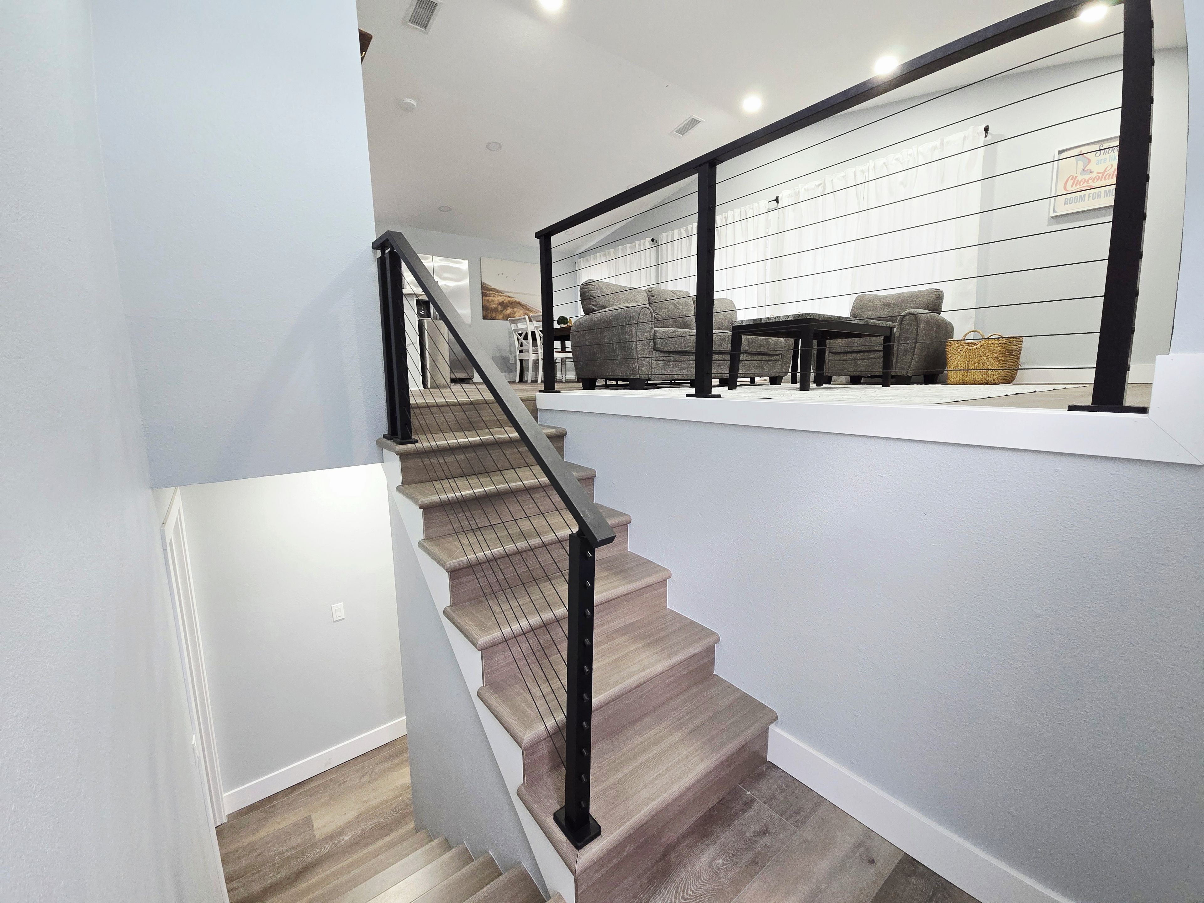 A staircase with a wooden finish and black railing leading to a living area with sofas and a coffee table.