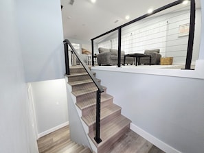 Eine Holztreppe mit schwarzer Geländer führt zu einem Wohnbereich mit Sofas und einem Couchtisch.