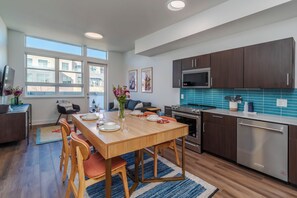 A modern kitchen with wooden cabinetry, stainless steel appliances, and a dining area with a wooden table and chairs. - Stunning FURNISHED 1BR/1BA Condo in Downtown Boulder - Digital Nomad's Dream (Boulder)